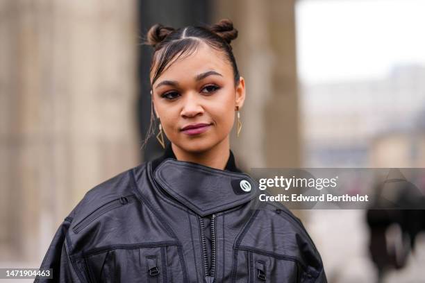 Madison Bailey wears gold earrings, a black shiny leather high neck / cropped biker jacket from Stella McCartney, outside Stella McCartney, during...