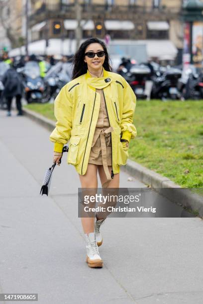 Yuwei Zhangzou wears yellow bomber jacket, beige skirt, button shirt, ankle boots, studded bag outside Stella McCartney during Paris Fashion Week -...