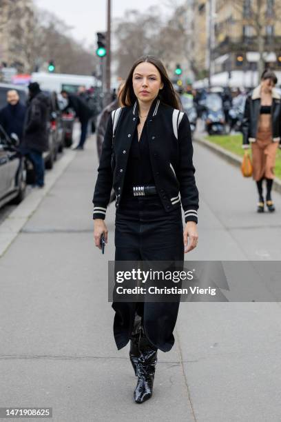 Guest wears black college jacket, black skirt with slit, black varnished bootsoutside Stella McCartney during Paris Fashion Week - Womenswear Fall...