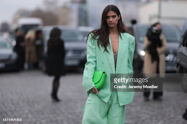 Sara Sampaio wears a pale green oversized blazer jacket, matching pale green wide legs pants, a neon green shiny leather handbag from Stella...