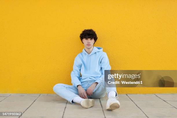 confident young man sitting on footpath in front of yellow wall - sitting on floor fotografías e imágenes de stock