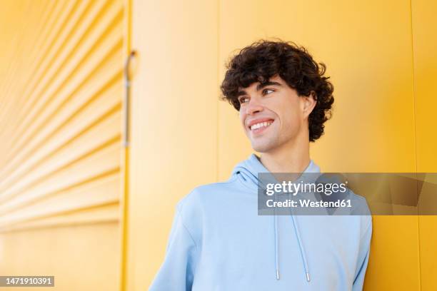 happy young man standing by wall - camisa con capucha fotografías e imágenes de stock