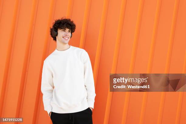 happy man wearing headphones in front of orange wall - sweatshirt imagens e fotografias de stock