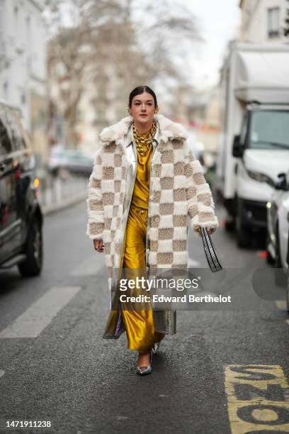 Guest wears gold large earrings, gold large chain necklaces, a yellow gold high neck silk long dress, a beige and white embossed checkered pattern...