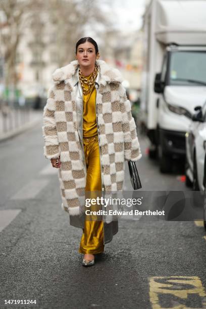 Guest wears gold large earrings, gold large chain necklaces, a yellow gold high neck silk long dress, a beige and white embossed checkered pattern...