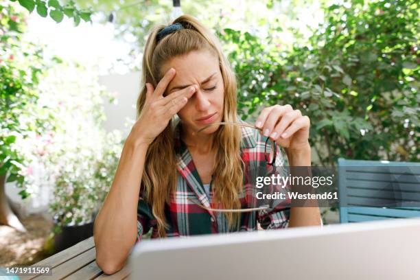 tired freelancer rubbing eye at table in back yard - rubbing eyes stock pictures, royalty-free photos & images