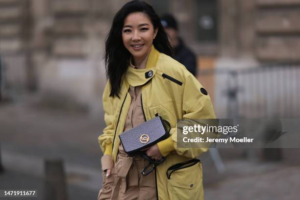 Yuwei Zhangzou wears yellow bomber jacket, beige skirt, button shirt, ankle boots, studded bag, outside Stella McCartney during Paris Fashion Week -...