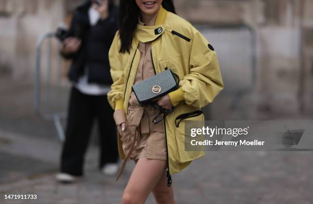 Yuwei Zhangzou wears yellow bomber jacket, beige skirt, button shirt, ankle boots, studded bag, outside Stella McCartney during Paris Fashion Week -...