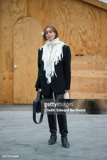 Guest wears a white lace print pattern fringed long scarf, a black blazer jacket, a black shiny leather handbag, black shiny leather pants, black...