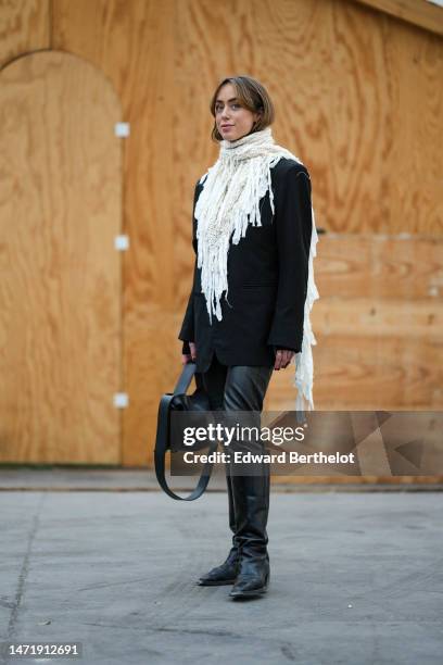 Guest wears a white lace print pattern fringed long scarf, a black blazer jacket, a black shiny leather handbag, black shiny leather pants, black...