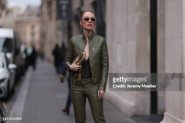 Viky Rader wears a khaki leather jacket with golden details and matching khaki leather pants, a black body with a wide cleavage, Tiffany and Co. Gold...