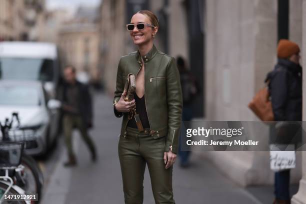 Viky Rader wears a khaki leather jacket with golden details and matching khaki leather pants, a black body with a wide cleavage, Tiffany and Co. Gold...
