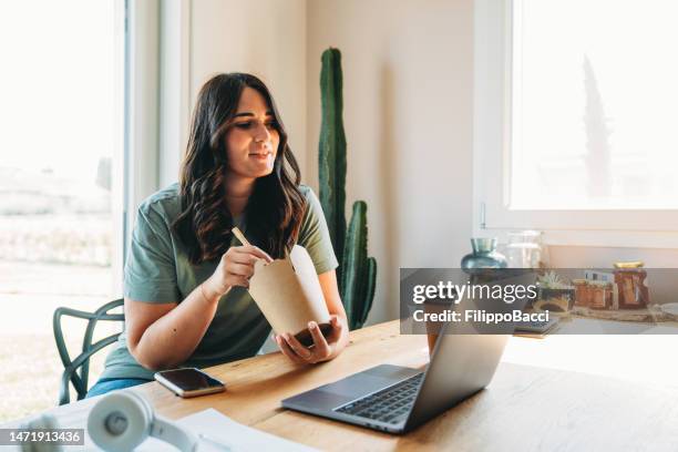 a woman is taking a lunch break while she's working from home with her laptop - lunch and learn stock pictures, royalty-free photos & images