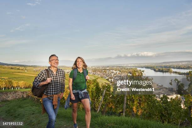 happy tourists hiking by vineyard under sky - rheingau stockfoto's en -beelden