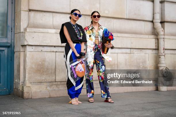 Guest wears red sunglasses, a gold LV logo earrings from Louis Vuitton, a gold large chain with logo pendant necklace from Louis Vuitton, a white...