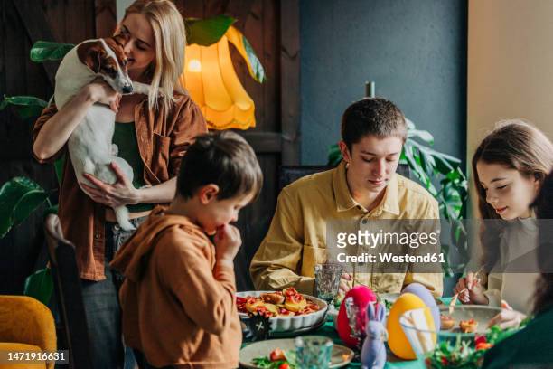happy woman holding dog with family having easter dinner at home - happy easter stock pictures, royalty-free photos & images