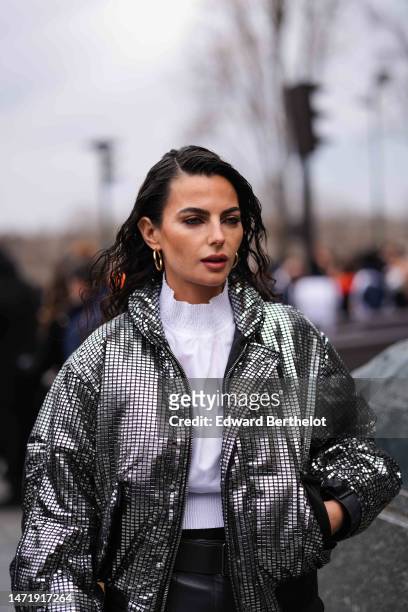 Guest wears gold earrings, a white ruffled high neck blouse, a black shiny leather with silver mirror embroidered bomber coat from Louis Vuitton, a...