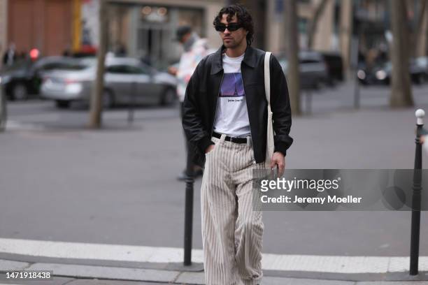 Yanis Serbout wears black sunglasses, a black leather jacket, a Palm Angels white t-shirt, a beige corduroy pants, a black leather belt and a beige...