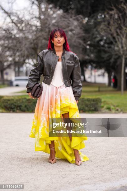 Guest wears gold earrings, a black faded denim zipper jacket, a white embossed pattern / shoulder-off / corset top, a pale orange to yellow gradient...