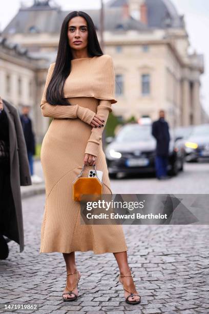 Guest wears gold earrings, a beige ribbed wool shoulder-off / long sleeves long midi tube dress, a camel suede handbag, black strappy heels sandals,...