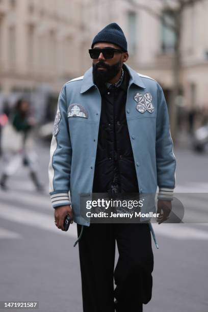 Jean-Claude wears black sunglasses, a blue hat, a Louis Vuitton blue leather jacket with white details, a black vest, a shirt with flower pattern, a...