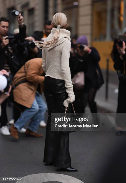 Caro Daur wears black sunglasses, a beige turtle neck pullover with long sleeves and golden buttoms details, ablack leather pants, black leather...