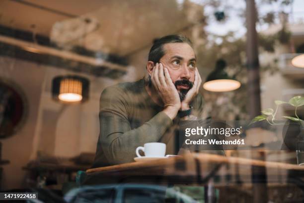 thoughtful mature man with hands on chin sitting in cafe - man looking up beard chin stock-fotos und bilder