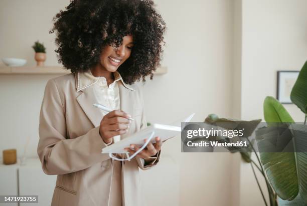 happy young businesswoman writing down notes in office - arab businesswoman with books stock-fotos und bilder