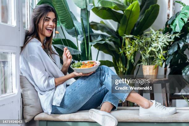 happy woman with bowl of salad at the window - young woman healthy eating stock-fotos und bilder