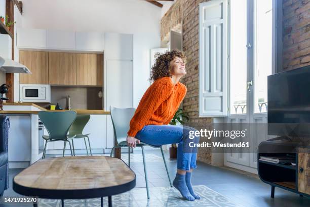 happy curly haired woman sitting on chair at home - woman excited sitting chair stock pictures, royalty-free photos & images