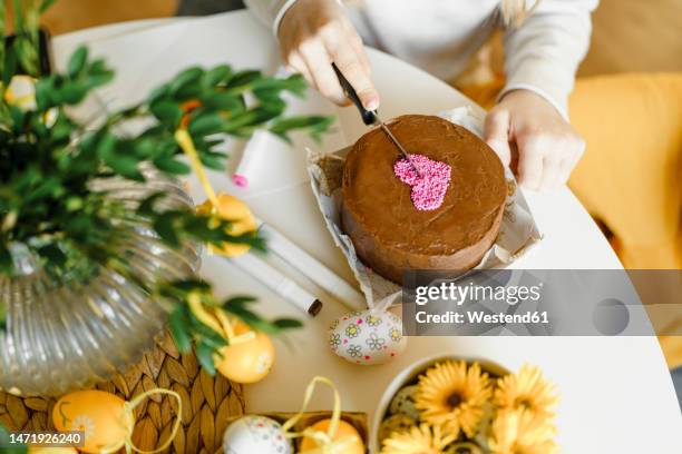 hands of girl cutting easter cake on table at home - paastaart stockfoto's en -beelden