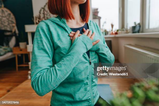 woman with hands on chest doing breathing exercise at home - manos sobre el pecho fotografías e imágenes de stock