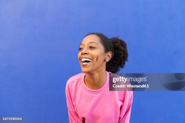 cheerful woman with afro hairstyle in front of blue background - grübchen stock-fotos und bilder