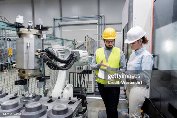 young engineer explaining colleague with machine part in factory - mechanical engineering drawing stock pictures, royalty-free photos & images