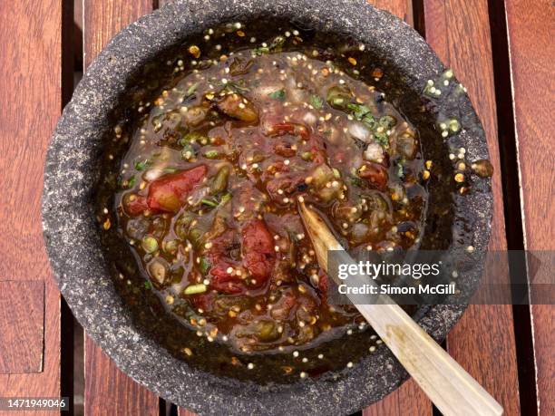 molcajete bowl of volcanic stone holding a ground spicy salsa of roasted tomatoes, tomatillos, onions, chili peppers and cilantro leaves - salsa sauce stock pictures, royalty-free photos & images