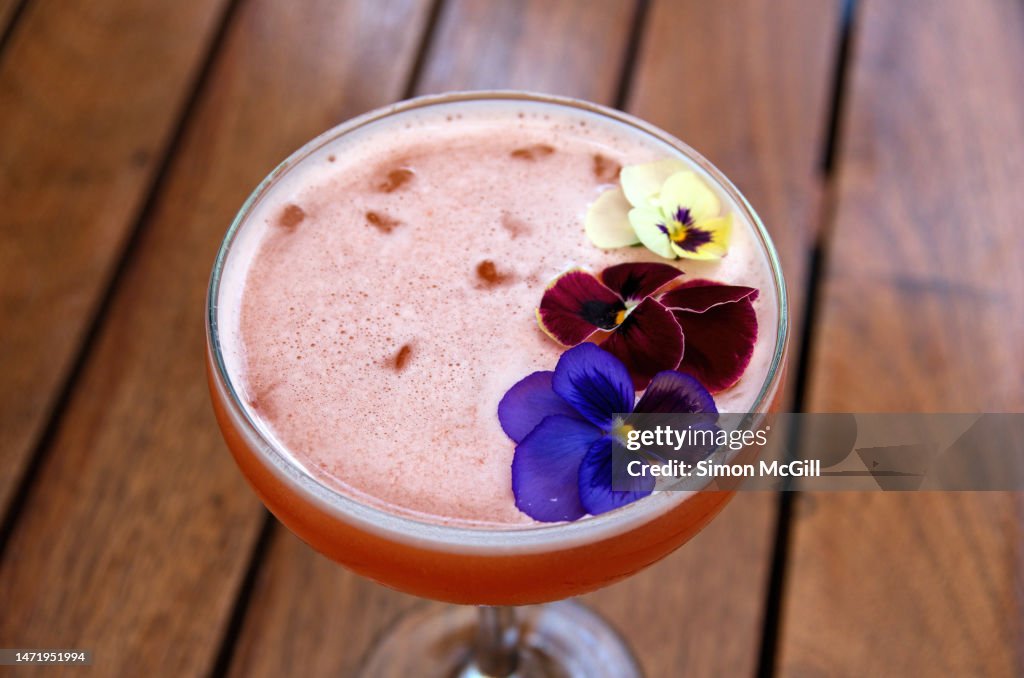 Alcoholic cocktail of gin, Aperol, pineapple juice, lime and pennyroyal mint, served in a champagne coupe glass and garnished with pansy flowers