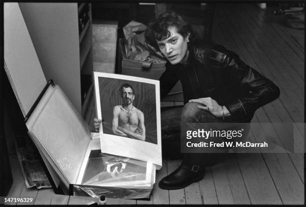 Portrait of American photographer as he poses with a portfolio of his photos in his loft studio , New York, New York, December 22, 1979.