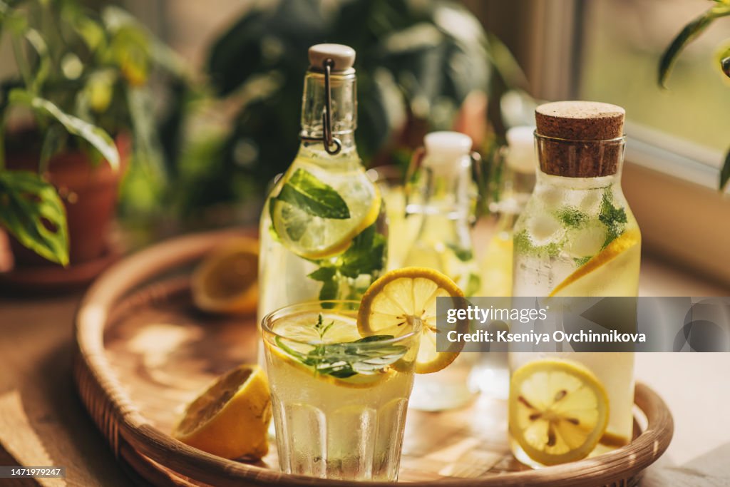 Lemonade in glass and bottle on wooden table outdoors. Summer refreshing drink. Cold detox water with lemon
