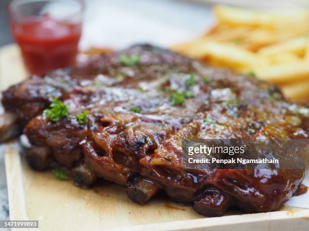 pork spareribs bbq, barbeque pork ribs with french fries vegetable salad, tomato sauce in a clear glass on wooden tray, food - smoked bbq ribs stock-fotos und bilder