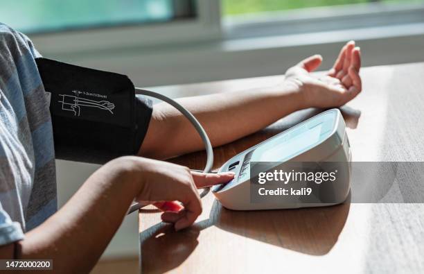 brazos de mujer midiendo la presión arterial en casa - indicador de presión sanguínea fotografías e imágenes de stock