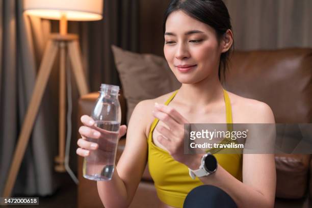 asian sport female woman taking capsule food suplement after working out at home, healthy diet. nutrition. vitamins. healthy eating - exercise pill stockfoto's en -beelden