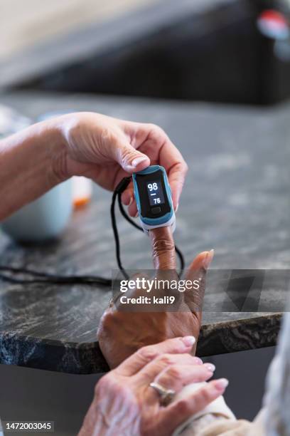hands of senior woman helping friend use pulse oximeter - medische artikelen stockfoto's en -beelden