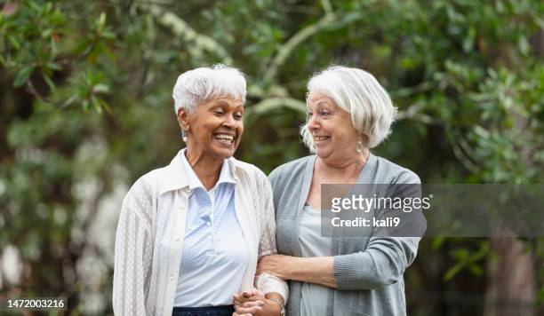 senior women walking, talking in back yard, smiling - two people talking outside stock pictures, royalty-free photos & images