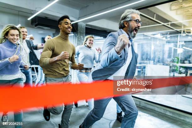 joyful businessman screaming while crossing the finish line during sports race with his colleagues in the office. - finish line stock pictures, royalty-free photos & images