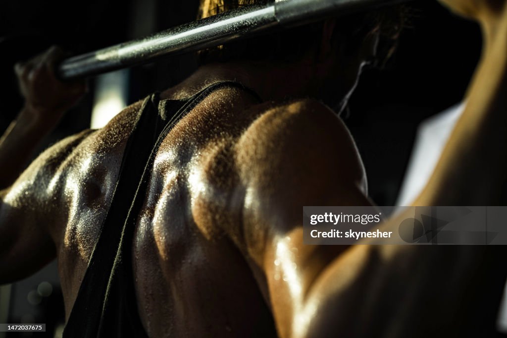 Close up of sweaty sportsman doing back exercises with barbell in a gym.
