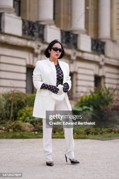 Guest wears black puffy sunglasses, a black with pale pink moon print pattern long sleeves gloves t-shirt from Marine Serre, a white blazer jacket,...
