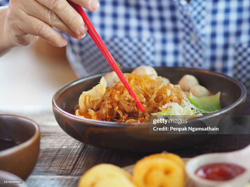 Woman uses a red fork to pick up noodles