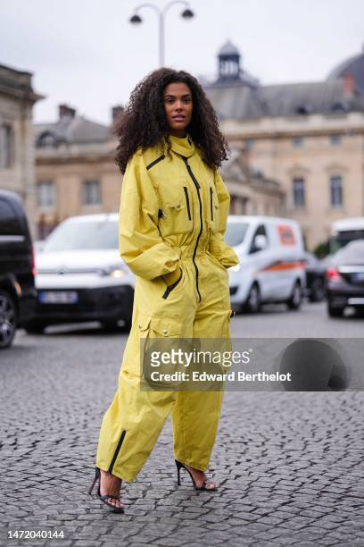 Guest wears a yellow high neck / puffy long sleeves / black zipper details cargo jumpsuit, black shiny leather heels strappy sandals , outside Stella...