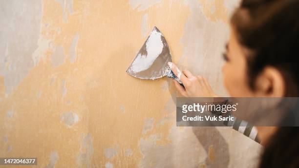 una donna che stacca una vernice dal muro - spatola foto e immagini stock