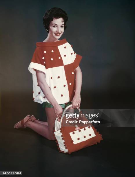 Posed studio portrait of a woman wearing a wide necked beach cover up top in large red and white checks with a pompom trim, with a matching beach bag...